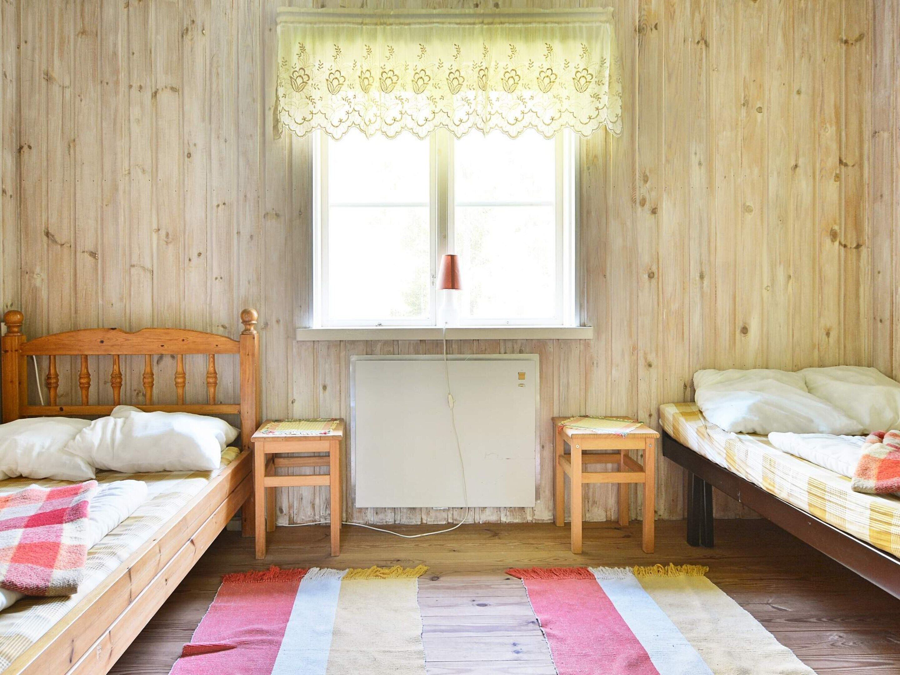 Une chambre avec deux lits en bois, un radiateur et une fenêtre ornée d’un rideau en dentelle.