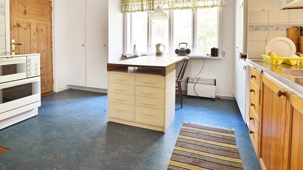 A kitchen with a central island, wooden cabinets, a window with a curtain, and a radiator. - 8 Person Holiday Home in Lonsboda (Lönsboda)