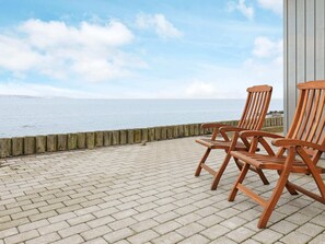 A wooden deck with two Adirondack chairs overlooking a body of water. - Seaside Escape in Hvalpsund - By Traum Ferienwohnungen (Farso)