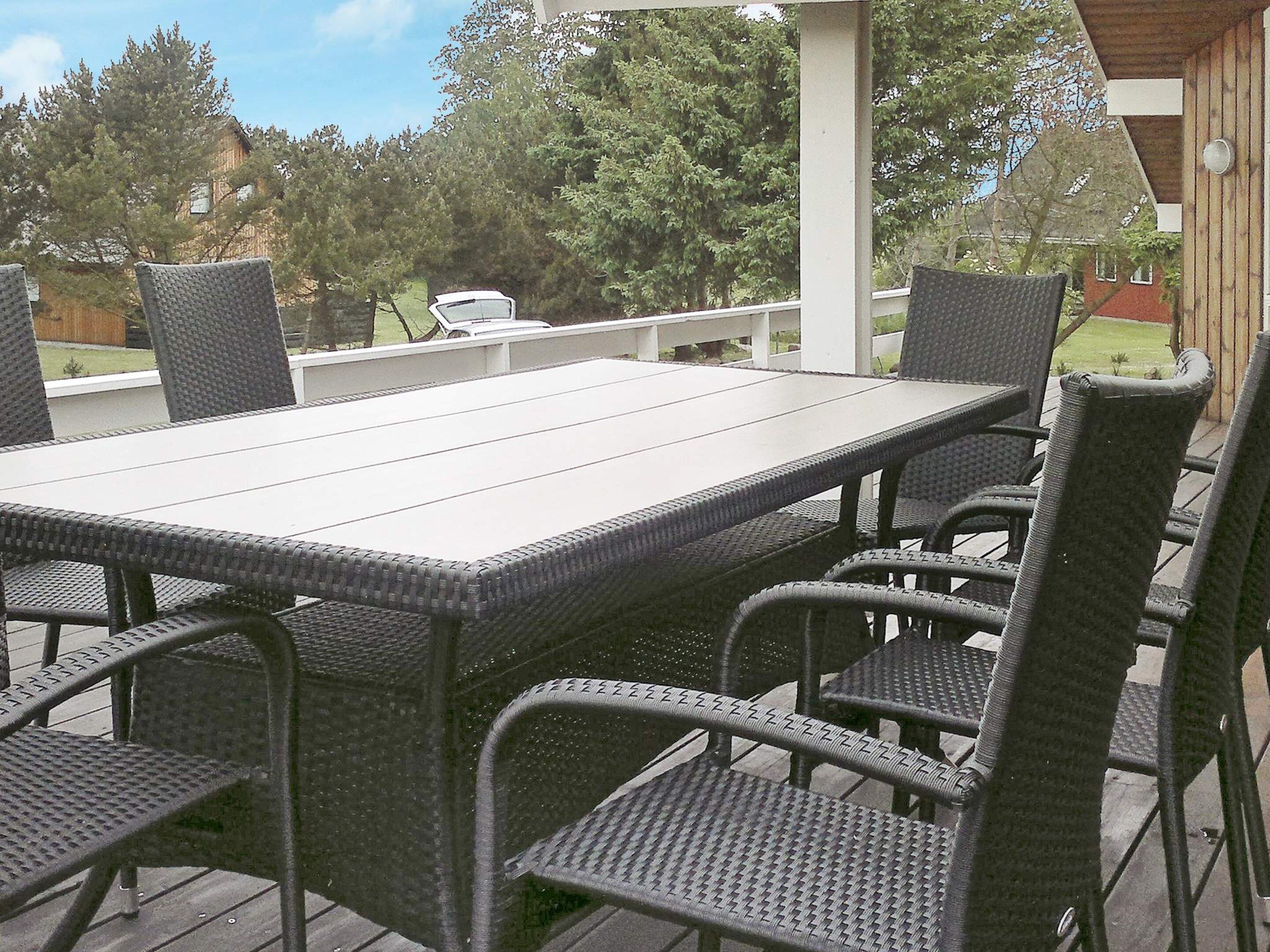 Een terras buiten met een rechthoekige tafel en zes stoelen.