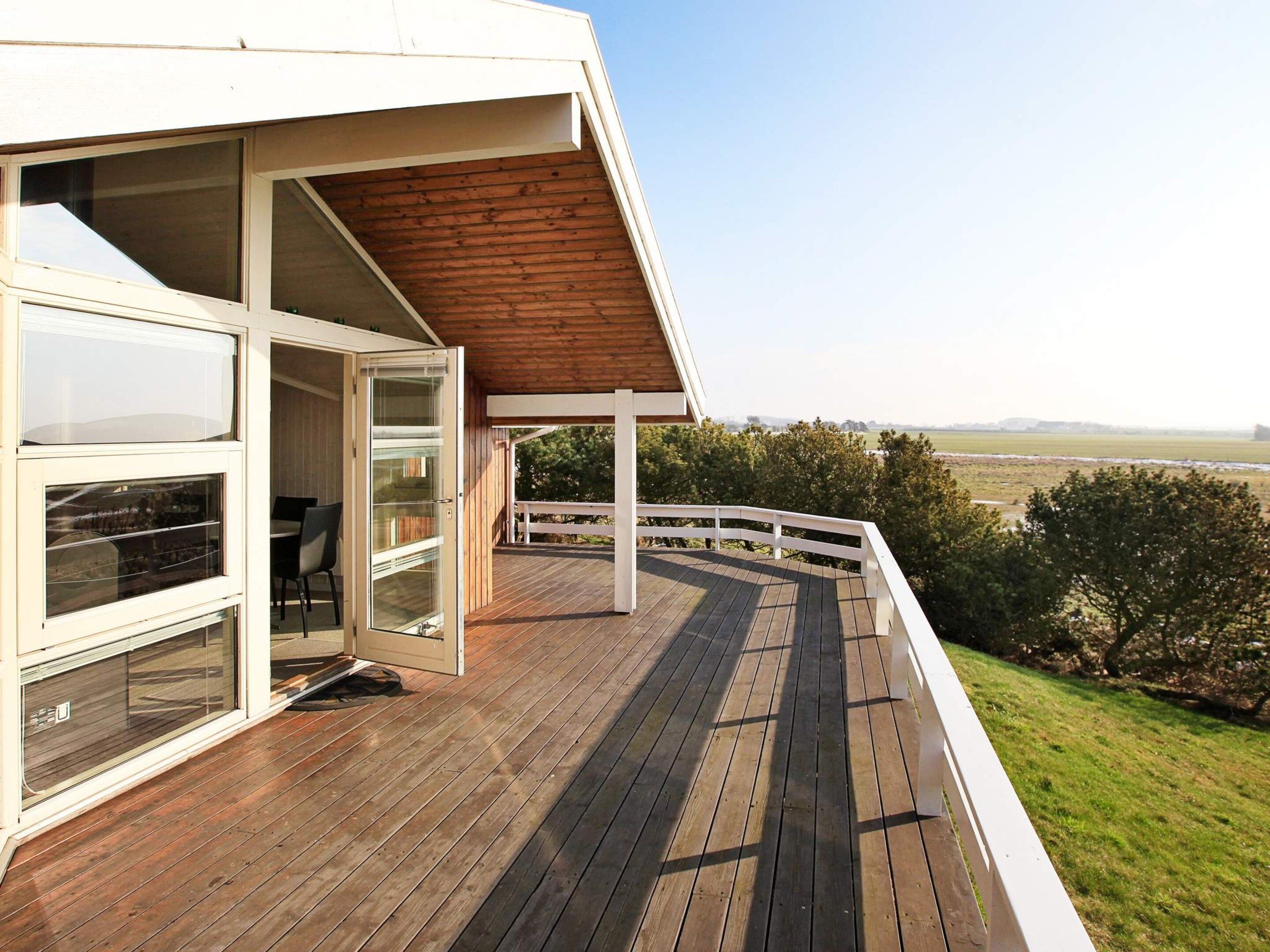 A wooden deck with a glass door leading to an interior space, a white railing, and a view of the landscape.