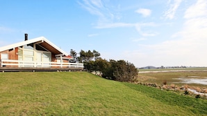 Een modern huis met een schuin dak, grote ramen en een terras met uitzicht op een grasveld.