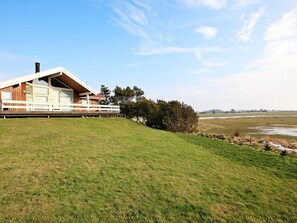 A modern house with a sloped roof, large windows, and a deck overlooking a grassy field.
