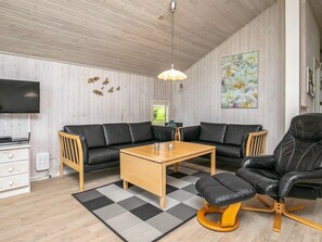 A modern living room with a sectional sofa, a coffee table, a black leather armchair, a wooden TV stand, and a mounted TV. - 4 Star Holiday Home in Humble (Sydlangeland)