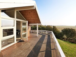 A wooden deck with a white railing, a glass door leading to a room, and a view of the landscape. - 4 Star Holiday Home in Humble (Sydlangeland)