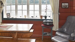 Una stanza con un tavolo di legno, una poltrona in pelle, una finestra vista lago e un piccolo ripiano con oggetti decorativi.