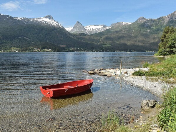 A red boat on a rocky shore with a lake and mountains in the background. - 10 Person Holiday Home in Folkestad (Volda)