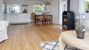 A modern kitchen with white cabinetry, a dining area with wooden furniture, and a black wood stove. - 6 Person Holiday Home in Struer-by Traum (Struer)