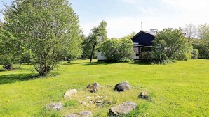 En græsplæne med enkelte sten, et lille skur og et hus med mørkt tag.
