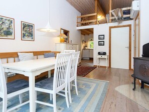 A room with a dining table, chairs, a bench, a sofa, a ceiling fan, a radiator, a door, and a small kitchen area.