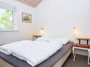A bedroom with a bed, two bedside tables, a bench, a window, and a wall-mounted picture.