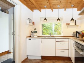 Una cocina con armarios blancos, lavavajillas integrado, ventana con vista a zonas verdes, luces colgantes y una estufa.