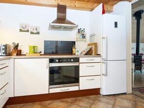 A compact kitchen with a stove, oven, and refrigerator, wooden ceiling beams, and a tiled floor.