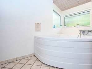 A bathroom with a large white bathtub, a window with a view, and a small plant on the windowsill. - 5 Star Holiday Home in Grenaa (Grenaa)