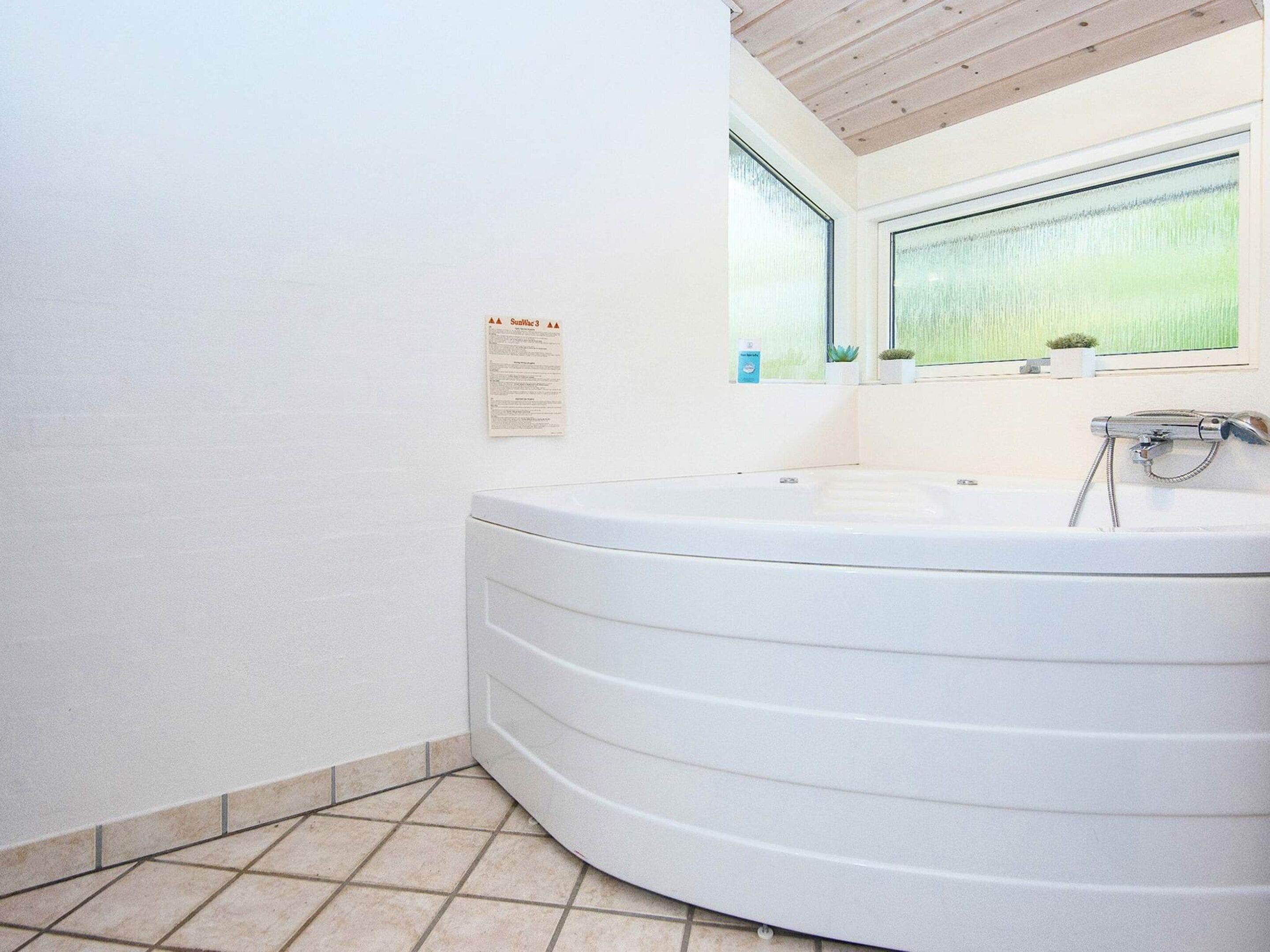 Une salle de bain avec une grande baignoire blanche, une fenêtre donnant sur un paysage verdoyant et une petite plante posée sur le rebord de la fenêtre.