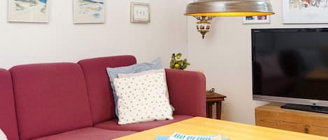 A living room with a red sofa, a wooden coffee table, a television, and wall art.