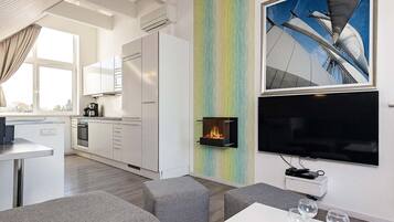 A modern kitchen with white cabinets, a built-in oven, and a dining area with grey sofas and a white table.