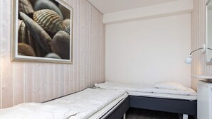 Un dormitorio pequeño y funcional con dos camas individuales, una pared de madera, un radiador blanco y un cuadro con caracolas.