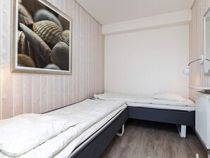 A small, compact bedroom with two single beds, a wooden wall, a white radiator, and a framed picture of shells. - Holiday Home in Wendtorf (Wendtorf)