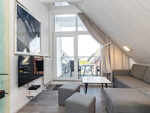 A modern loft bedroom with a large window, a flat-screen TV, a sofa, and a small table.