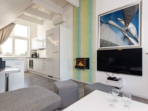 A modern kitchen with white cabinets, a built-in stove, and a dining area with grey sofas and a white table. - Holiday Home in Wendtorf (Wendtorf)