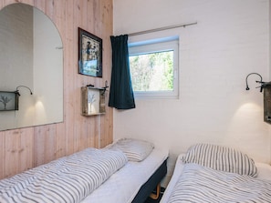 A room with two single beds, a large mirror, a framed picture, a window with a curtain, and a wall-mounted light fixture. - Cozy Holiday Home in BlÃ¥vand near Beach (Blavand)