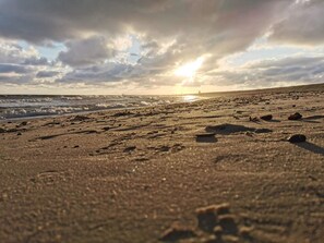 A beach with footprints and rocks, and the sun is setting in the background. - Cozy Holiday Home in BlÃ¥vand near Beach (Blavand)