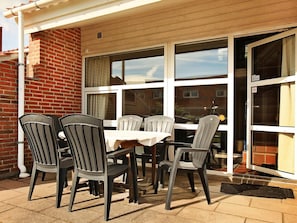 Une terrasse extérieure avec une table et des chaises, un mur en briques et une porte-fenêtre coulissante.