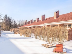 Une rangée de bâtiments en briques surmontés de toits de tuiles rouges, un sol recouvert de neige et des arbres sans feuilles.