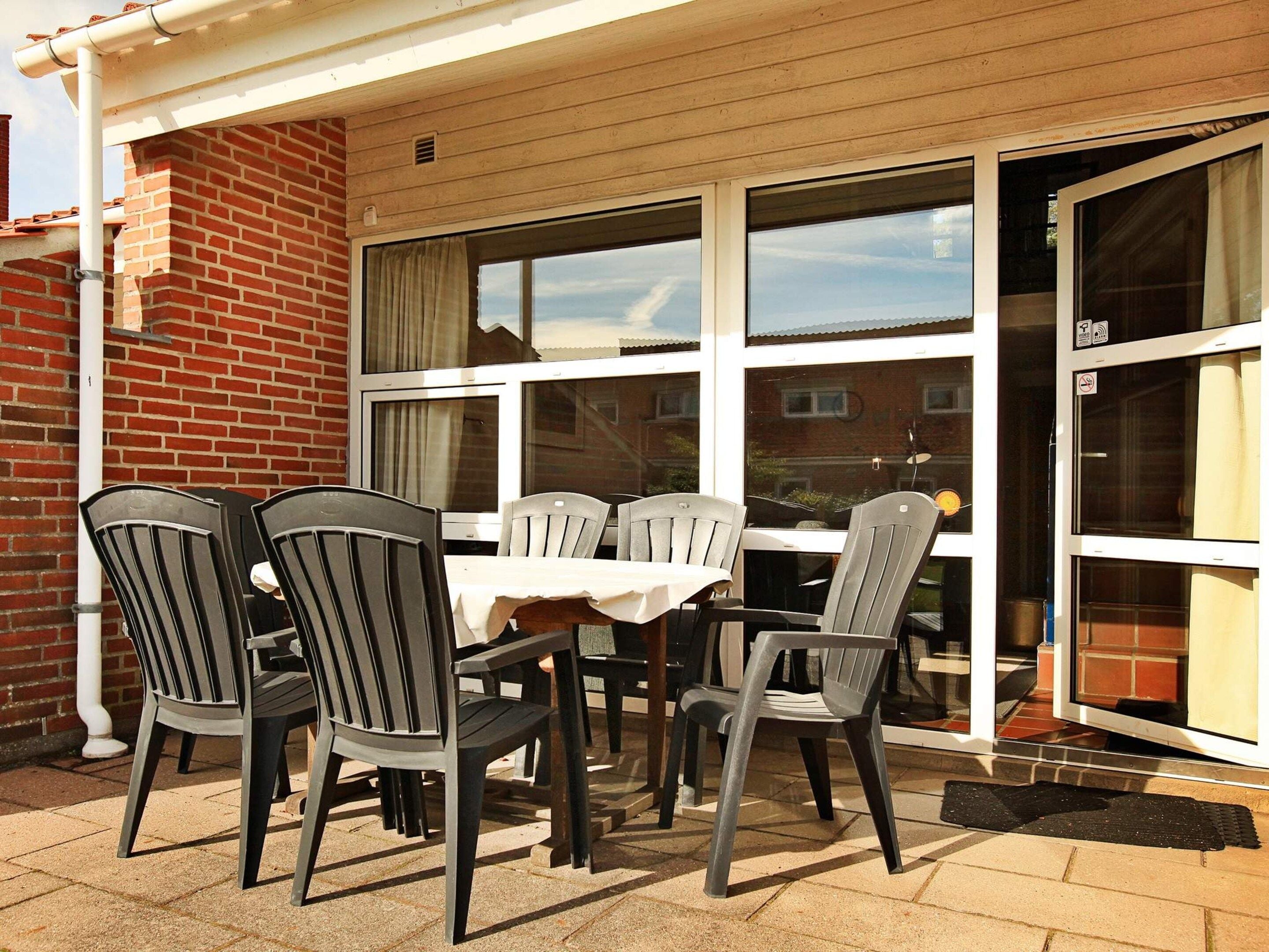 An outdoor patio with a table and chairs, a brick wall, and a sliding glass door.
