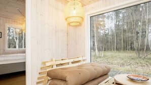 A cozy room with a wooden bench, a round table, and a large window offering a view of a forest. - 2 Person Holiday Home in Laeso-by Traum (Læsø)