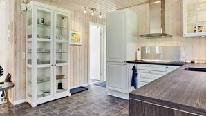 A modern kitchen with wooden paneling, a large cabinet with glass doors, a gas stove, and a stainless steel range hood. - 2 Person Holiday Home in Laeso-by Traum (Læsø)