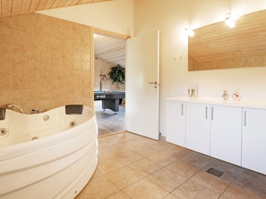 A modern bathroom with a freestanding bathtub, a sink with a mirror, and a door leading to a pool table area. - 5 Star Holiday Home in Albaek (Aalbaek)