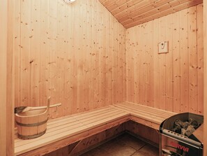A sauna room with wooden walls and benches, a wooden bucket, and a sauna heater. - 5 Star Holiday Home in Albaek (Aalbaek)