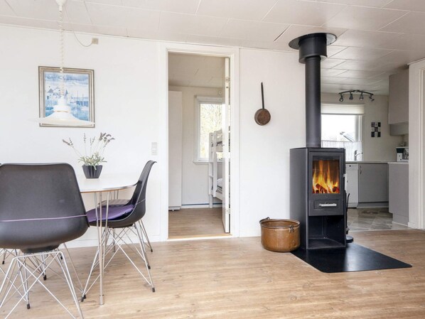 Una sala de estar moderna con un estufa de leña negra, una mesa de comedor con sillas y vistas a la cocina.