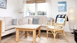 A living room with a sofa, a wooden table, a wicker chair, and a window with curtains.