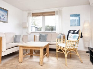 A living room with a sofa, a wooden table, a wicker chair, and a window with curtains.