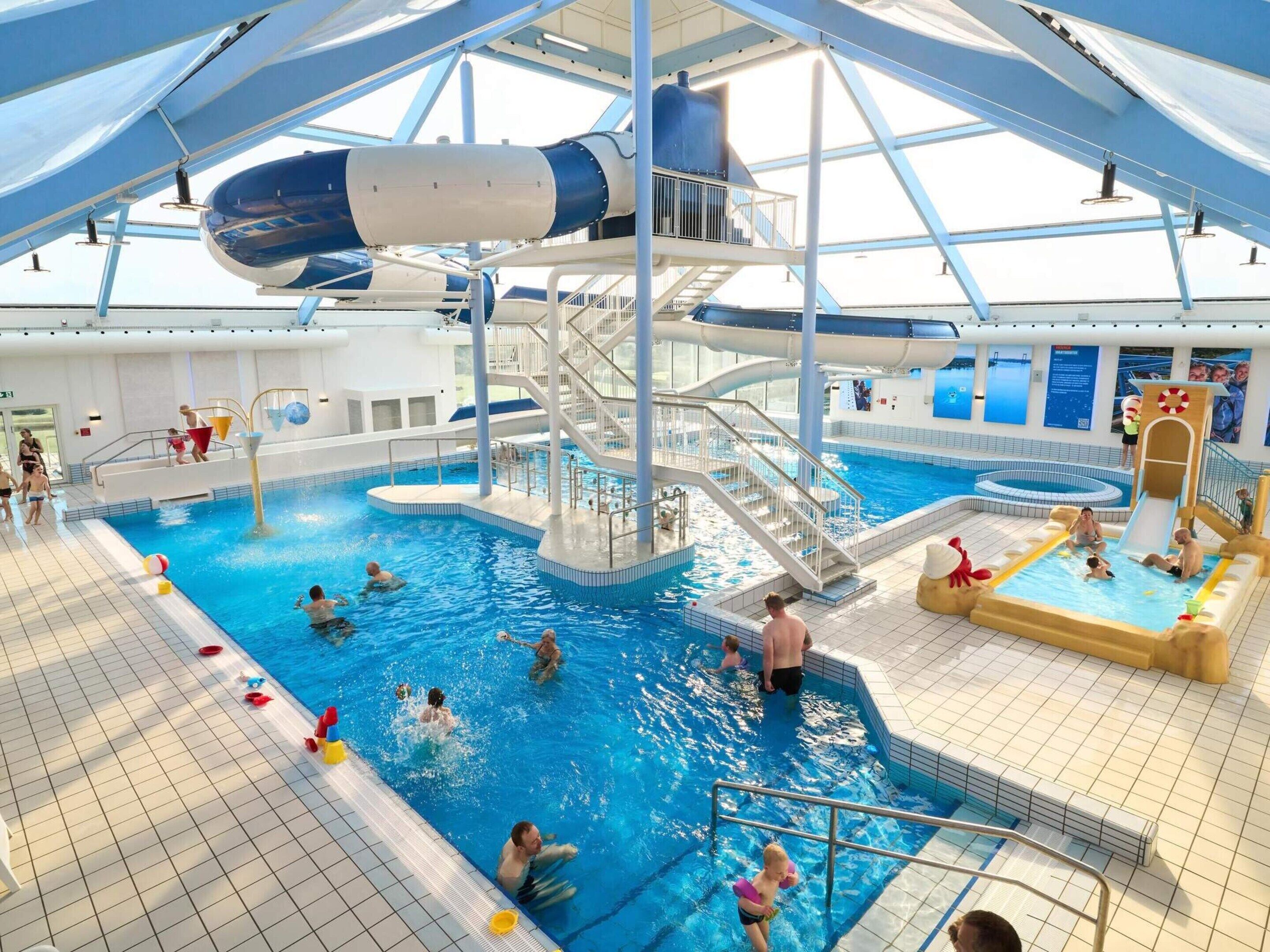 An indoor swimming pool with a water slide, multiple lanes, and a lifeguard stand.