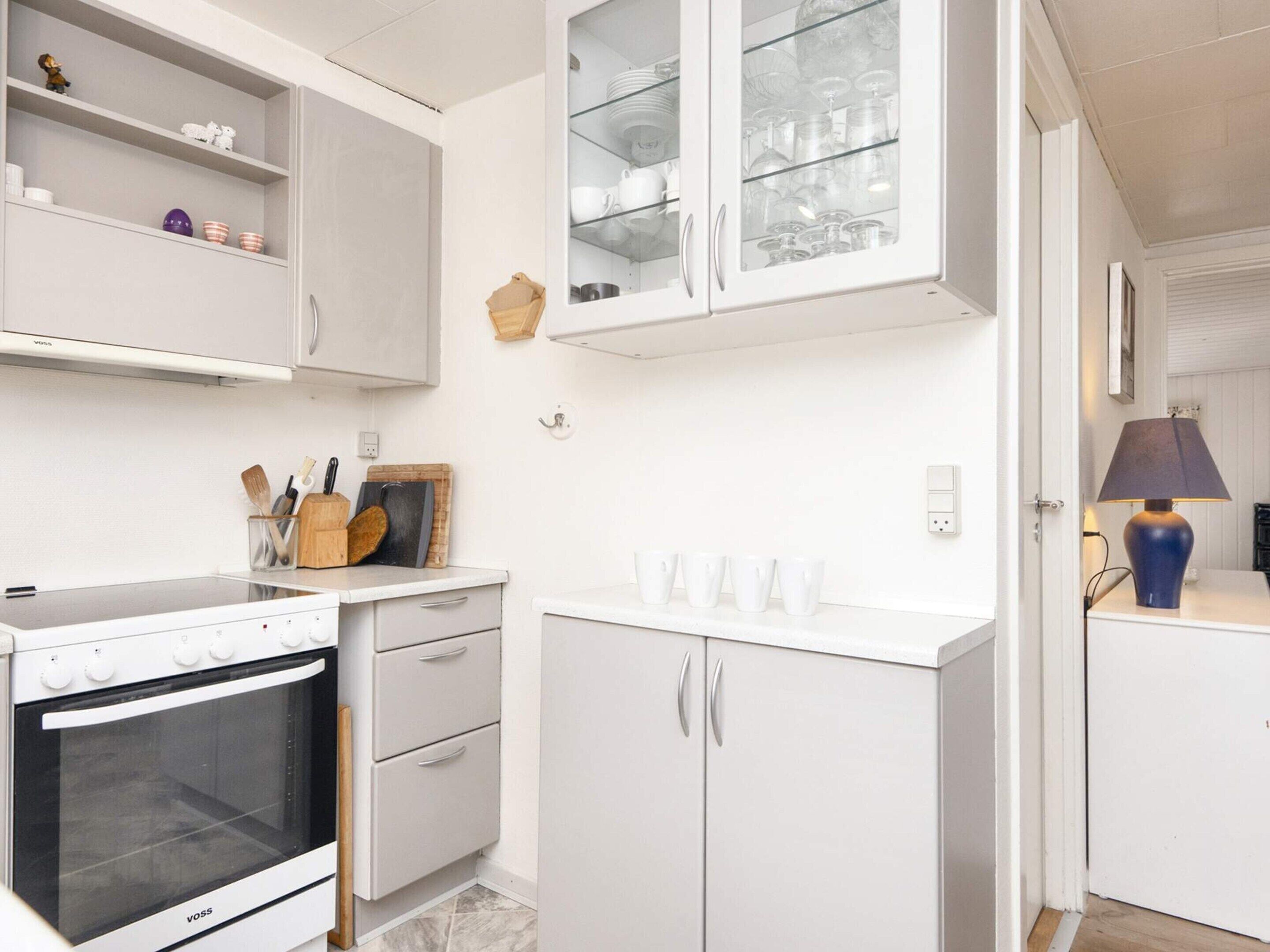 Una cocina con armarios blancos, horno empotrado y encimera con utensilios de cocina.