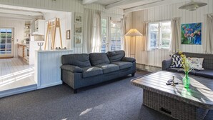 A spacious living room with a grey sofa, a wicker coffee table, and a painting on the wall. - 6 Person Holiday Home in Rodby (Rodby)