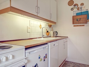 A kitchen with white cabinets, a wooden countertop, a stove, a dishwasher, and a wall-mounted rack with kitchen items.