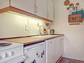 A kitchen with white cabinets, a wooden countertop, a stove, a dishwasher, and a wall-mounted rack with various items. - Quaint Holiday Home in LÃ¸kken With Beach Nearby (Gudhjem)