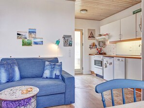 A modern kitchen with white cabinets, a stove, and a dishwasher. There is a blue sofa with a round coffee table in the living area. - Quaint Holiday Home in LÃ¸kken With Beach Nearby (Gudhjem)
