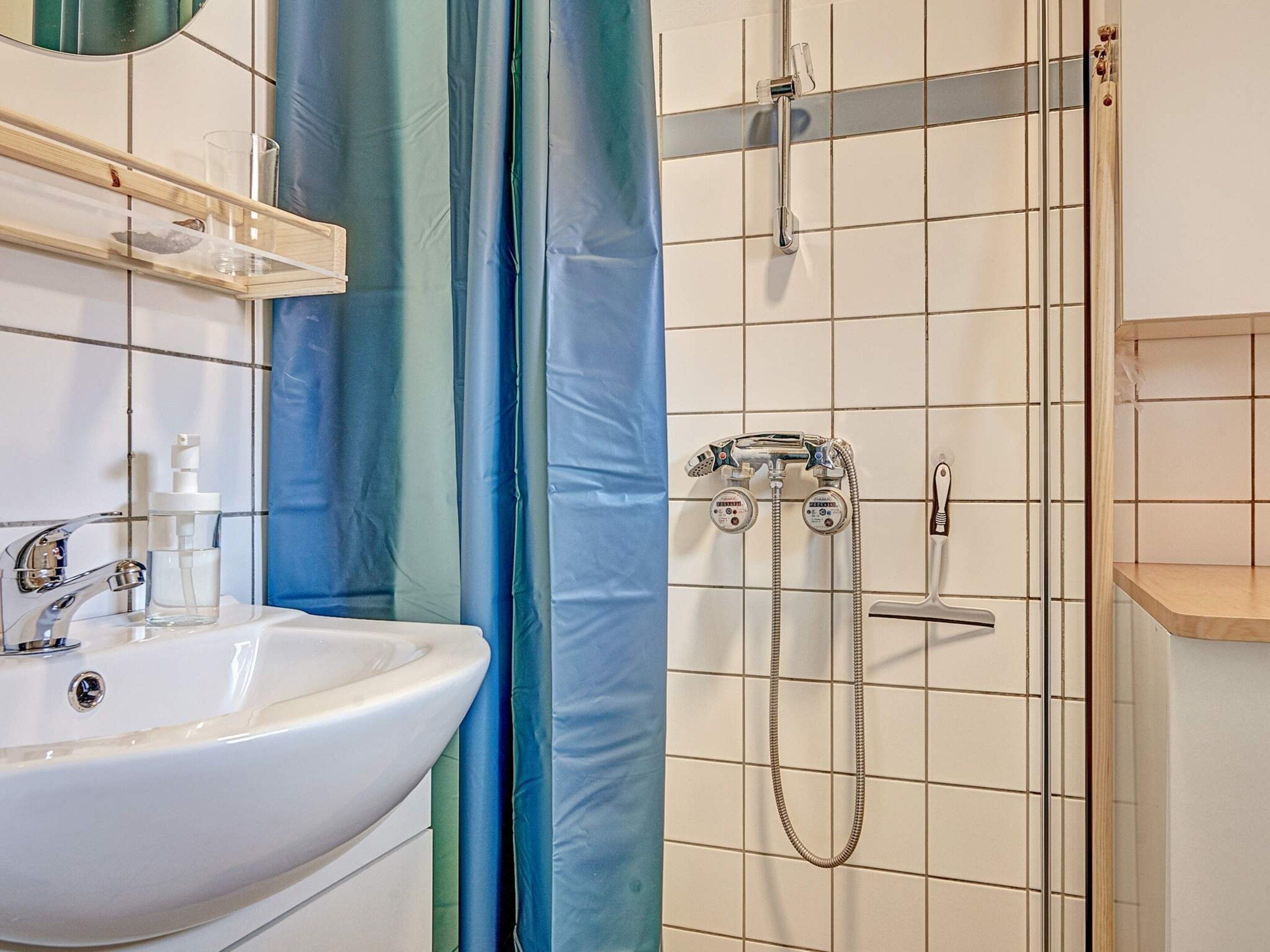Ein Badezimmer mit einem weißen Waschbecken, einem Spiegel, einer Dusche mit Duschbrause und einem blauen Duschvorhang.