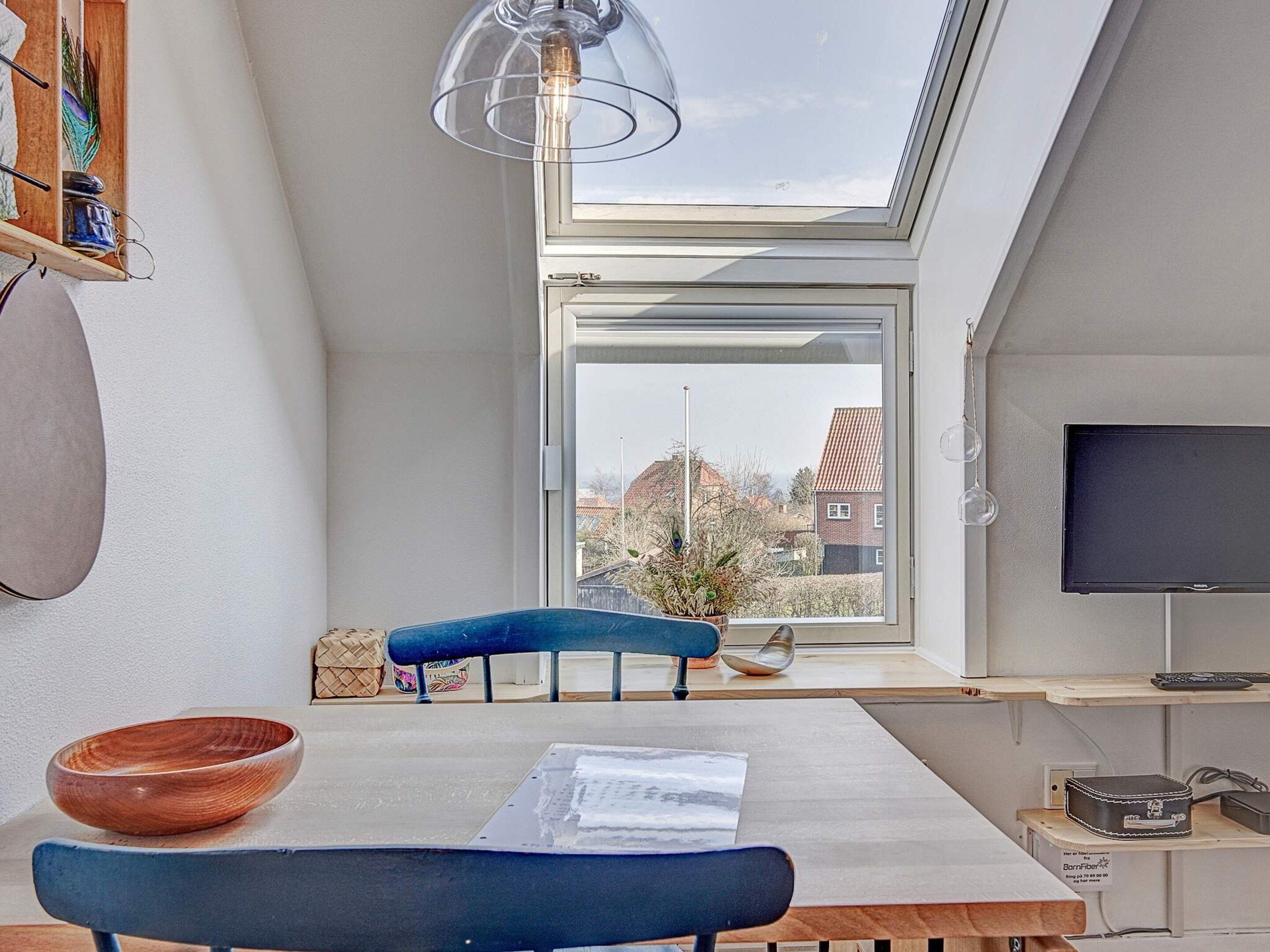 Une pièce moderne avec une lucarne, une table à manger avec un saladier, une chaise, un banc bleu et un téléviseur.