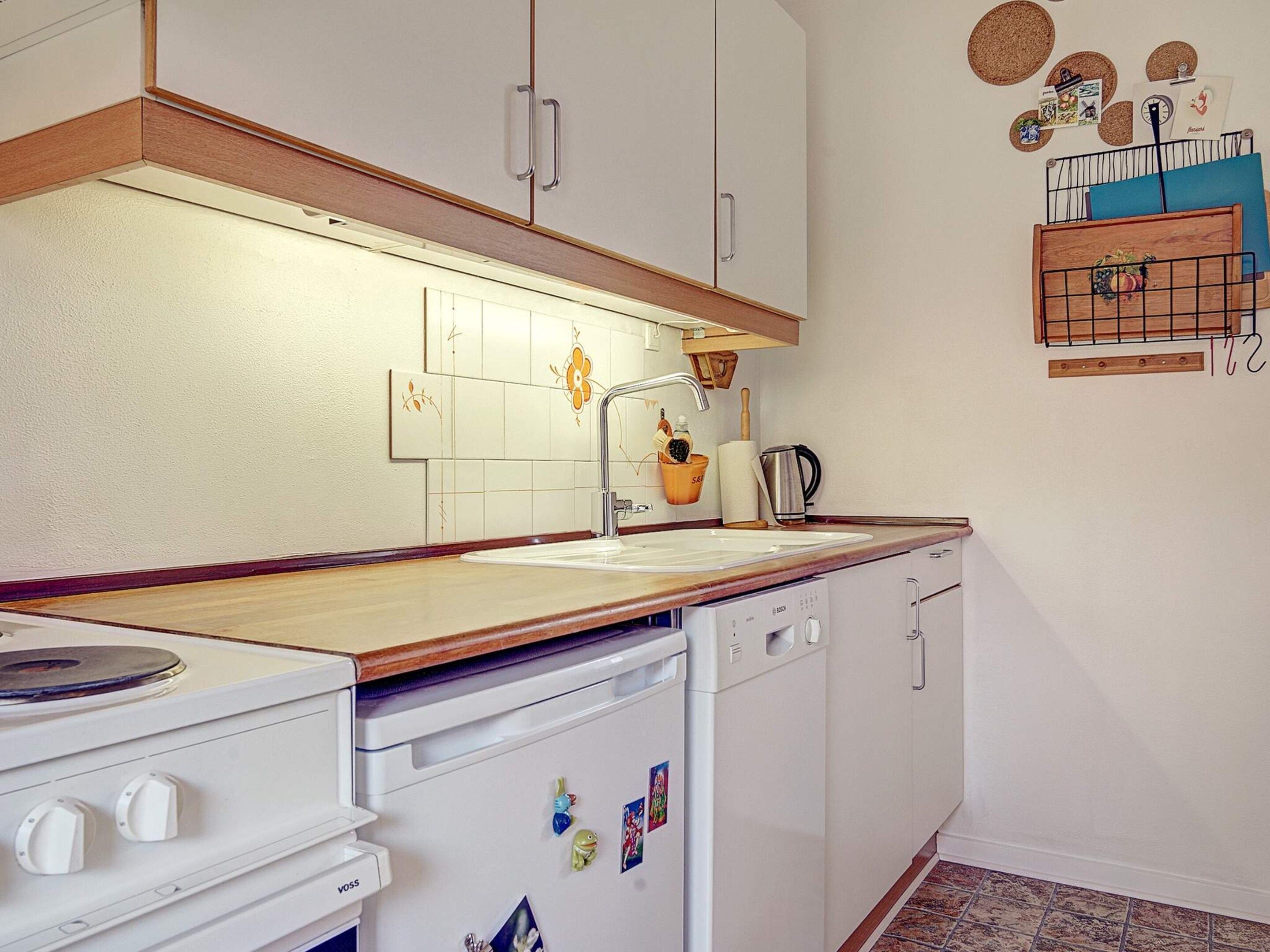 A kitchen with white cabinets, a wooden countertop, a stove, a dishwasher, and a wall-mounted rack with kitchen items.