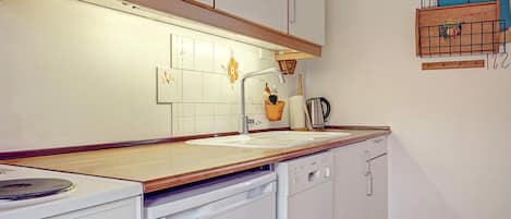 A kitchen with white cabinets, a wooden countertop, a stove, a dishwasher, and a wall-mounted rack with kitchen items.