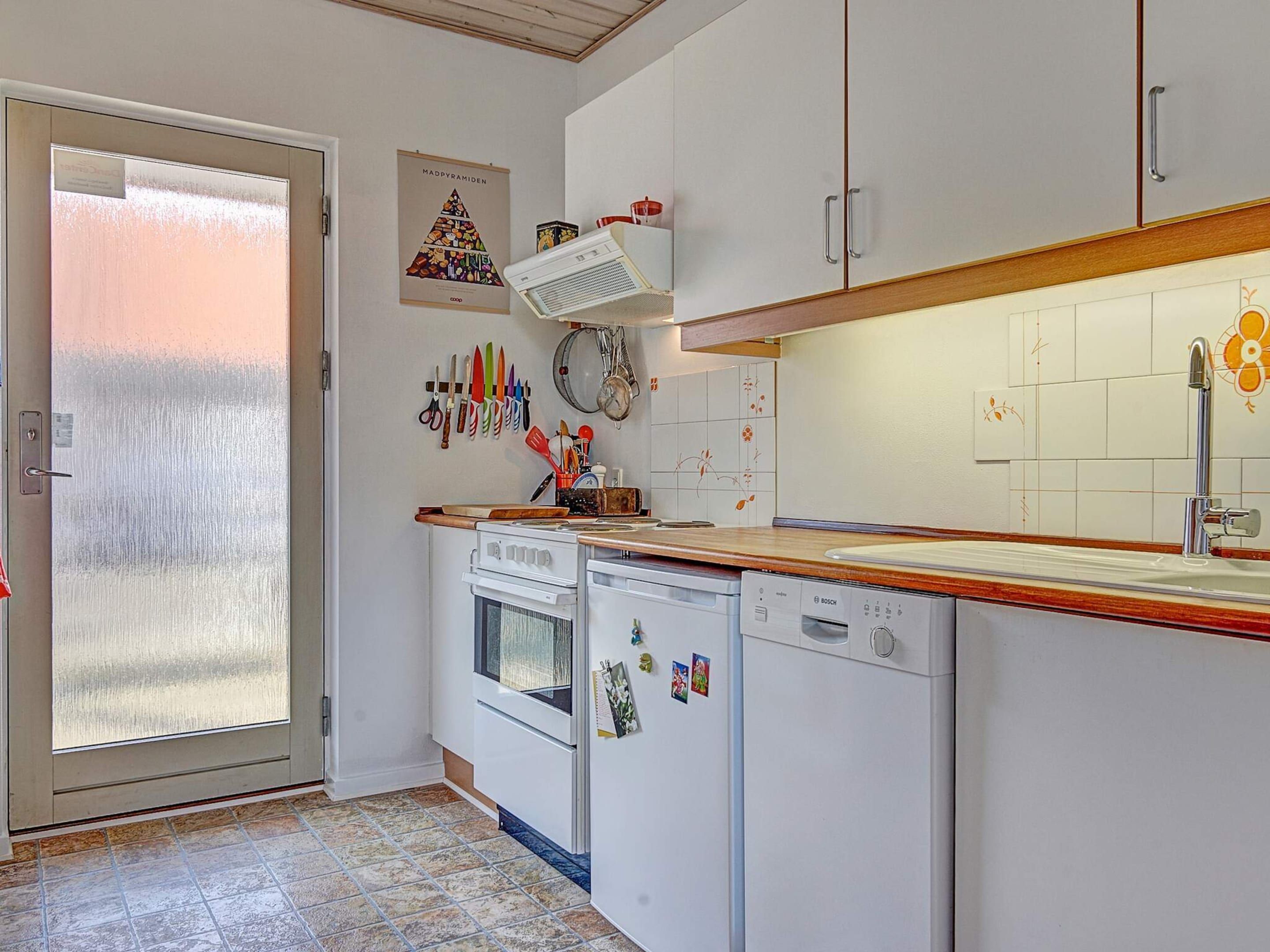 Cocina compacta con armarios blancos, horno integrado, lavavajillas y pileta de acero inoxidable.