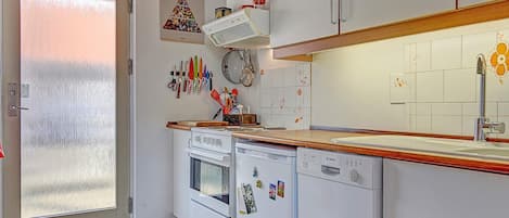 Cocina compacta con armarios blancos, horno integrado, lavavajillas y pileta de acero inoxidable.