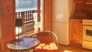 A cabin interior with a kitchen, a dining area with a table and chairs, and a view of a lake through a large window. - 8 Person Holiday Home in Etne (Etne)